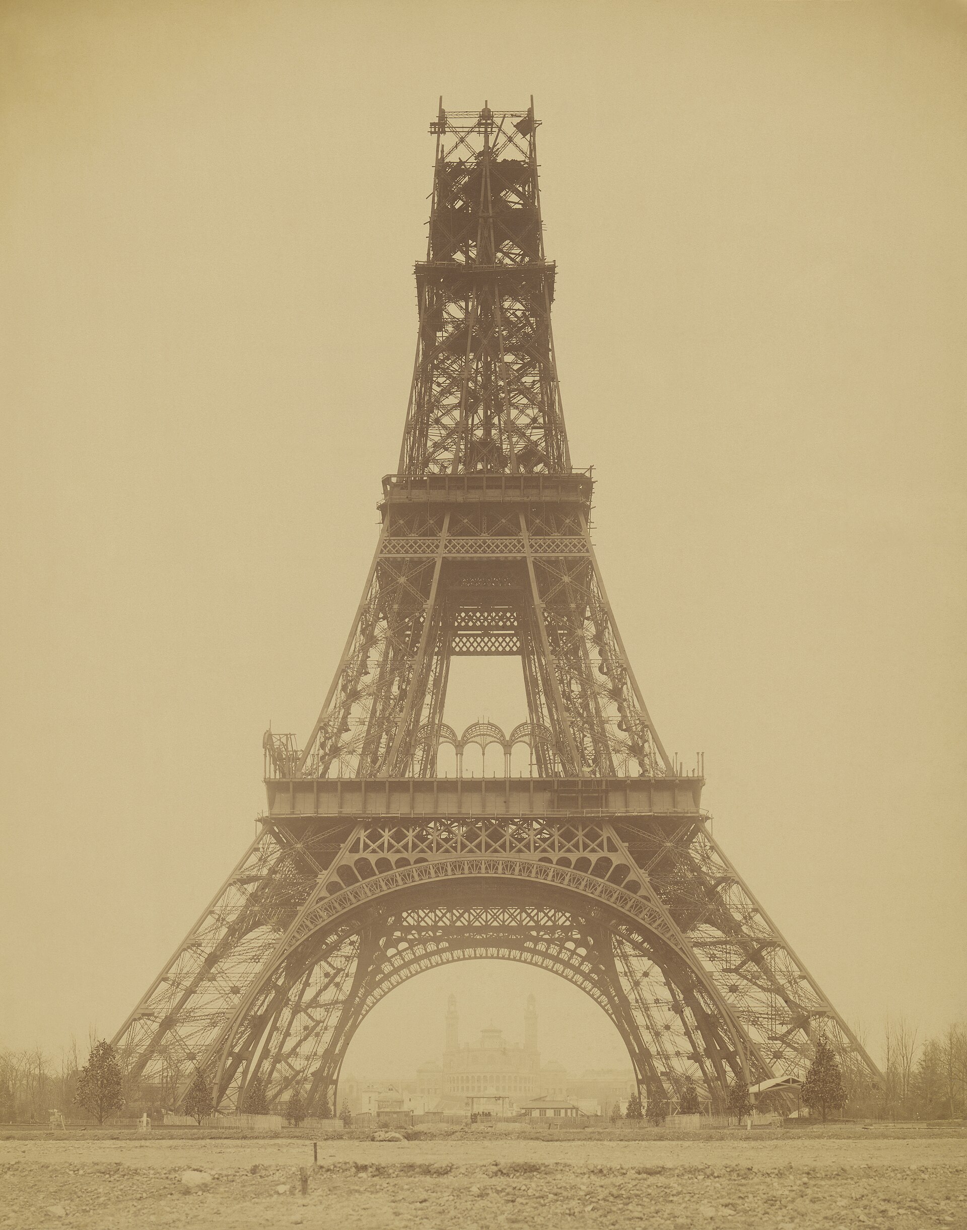 The Eiffel Tower part-built, its four legs rising above the Paris rooftops in 1888